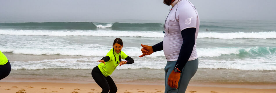 Professional surf instructor teaching proper pop-up technique to student on beach