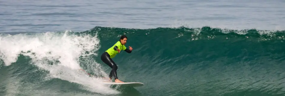 Female surfer in yellow rashguard trimming along green wave face