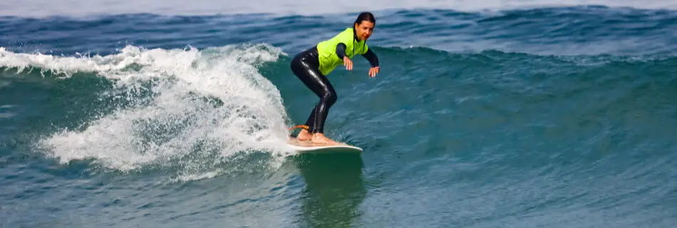 Female surfer in yellow rashguard riding green wave with perfect stance