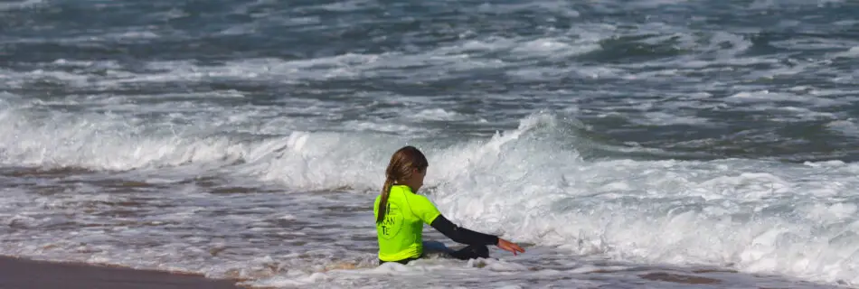 Young surfer in neon yellow wetsuit playing in ocean waves