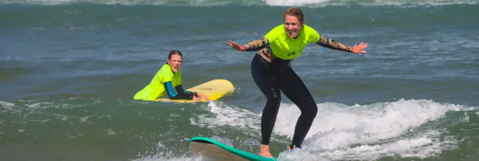 Mother and child surfing together, both riding waves in bright yellow rashguards