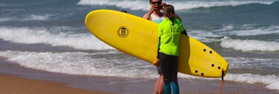 Father taking photo of child surfer with yellow softboard on beach