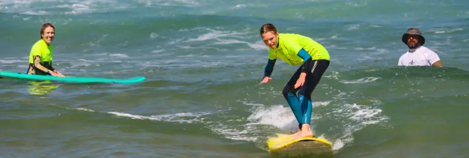 Family surf lesson with instructor - child riding wave while parent and instructor watch