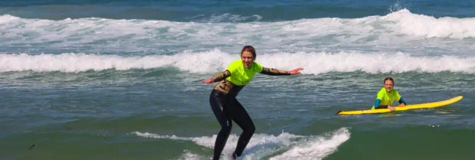 Mother surfing wave while child watch and cheer from the water