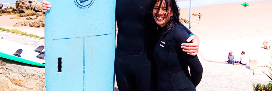 Couple holding surfboard together and smiling before their surf lesson