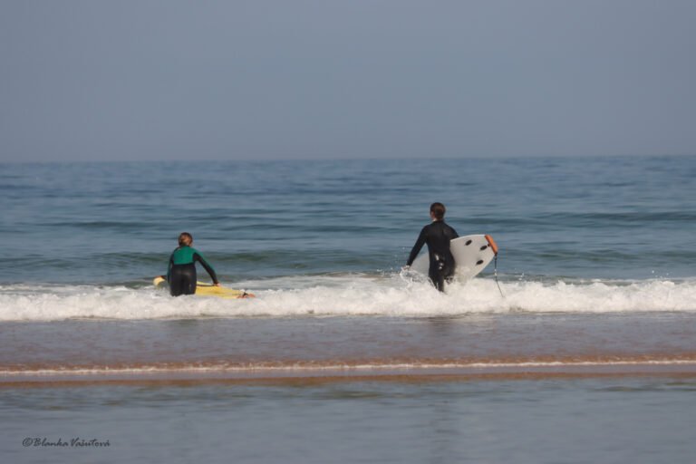 Pláže s modrou vlajkou u Santa Cruz: co vlajka znamená a kde ji najdeš 1 Two surf students walking into the sea with their boards